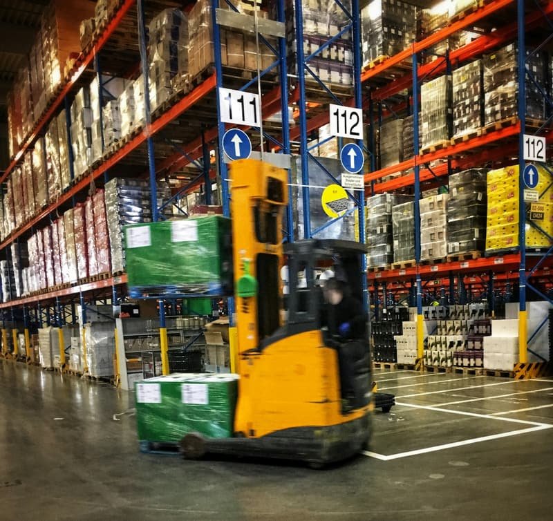Order picker moving stock between tall warehouse racking